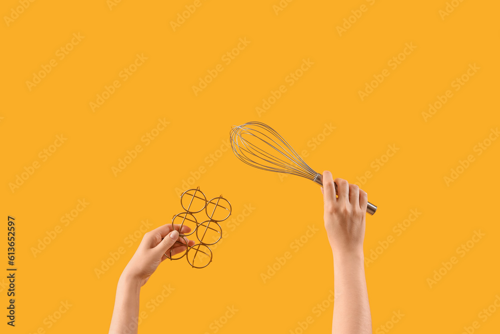 Female hands holding whisk and egg holder on yellow background