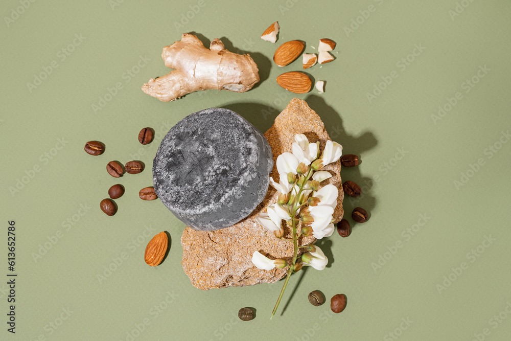 Grey solid shampoo bar with flower, ginger and coffee beans on green background