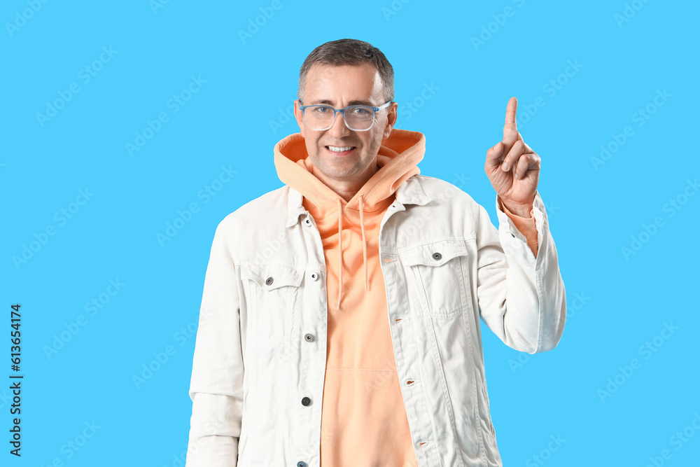 Mature man in eyeglasses pointing at something on blue background