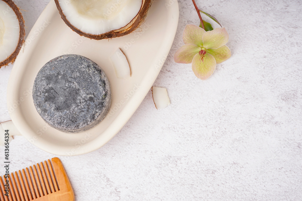 Stand with handmade solid shampoo, coconut, orchid flower and hair comb on light background