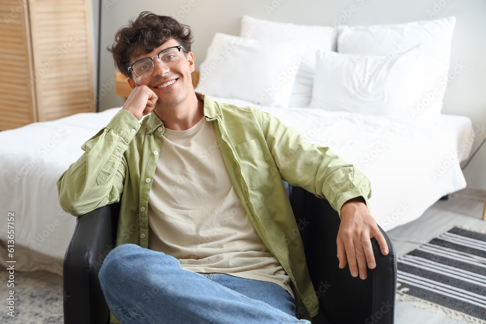 Young man with eyeglasses sitting in bedroom