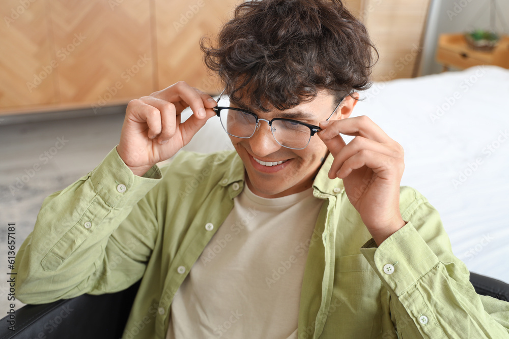 Young man with eyeglasses sitting in bedroom, closeup