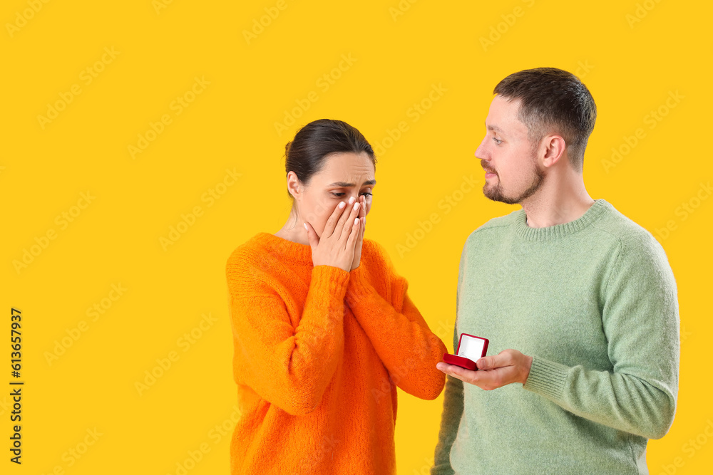 Young man proposing to his girlfriend on yellow background