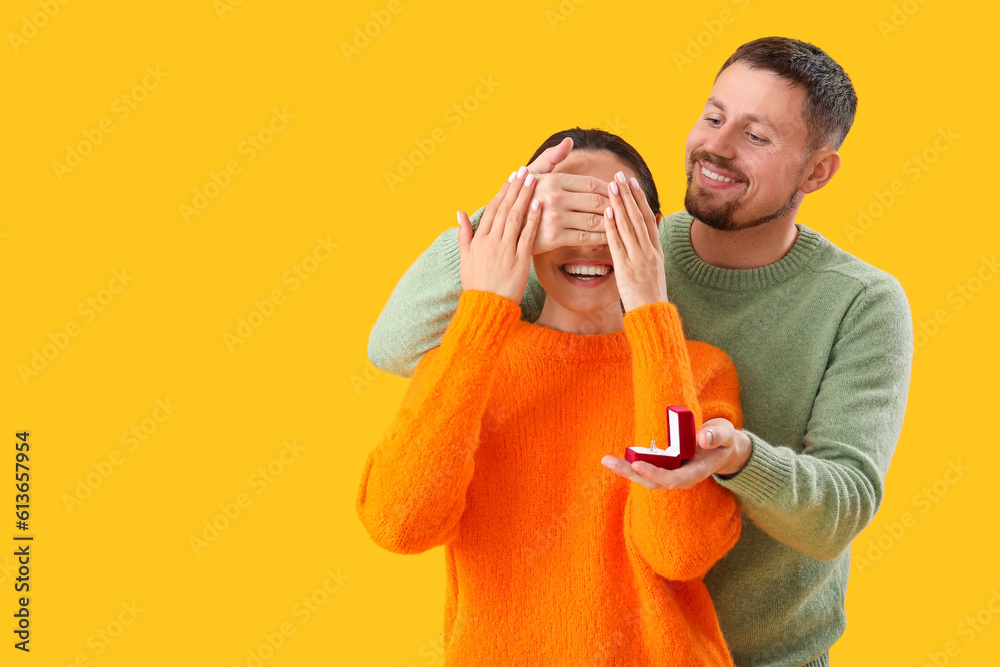 Young man proposing to his girlfriend on yellow background