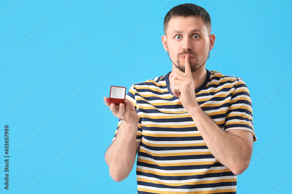 Handsome man with engagement ring showing silence gesture on blue background