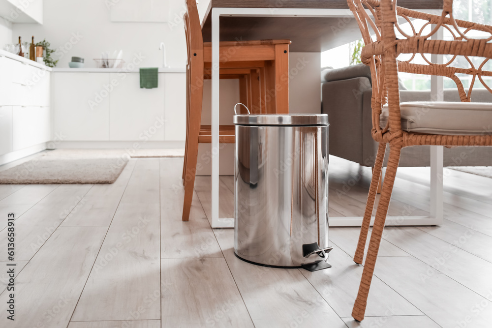 Metallic trash bin near table in interior of modern kitchen