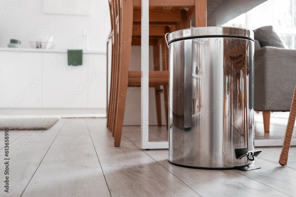 Metallic trash bin near table in interior of modern kitchen