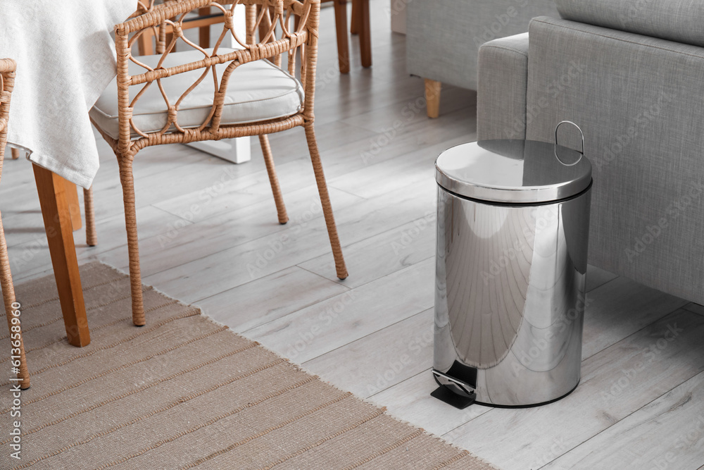 Metallic trash bin near sofa in interior of modern kitchen