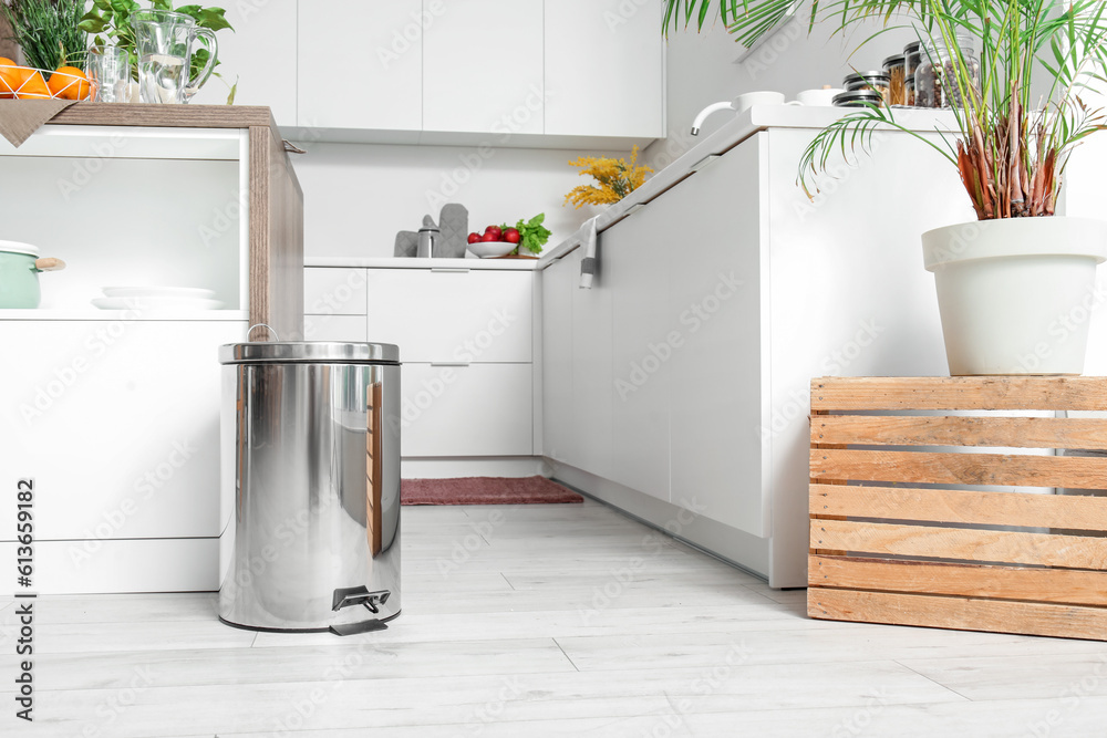 Metallic trash bin near table in interior of modern kitchen