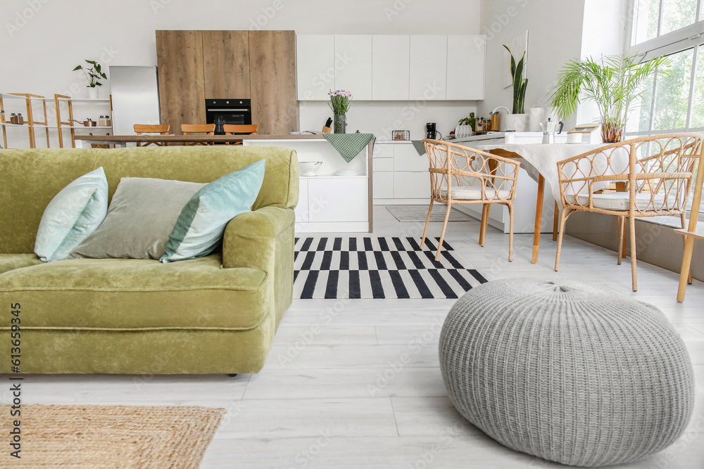 Interior of light open plan kitchen with green sofa and pouf