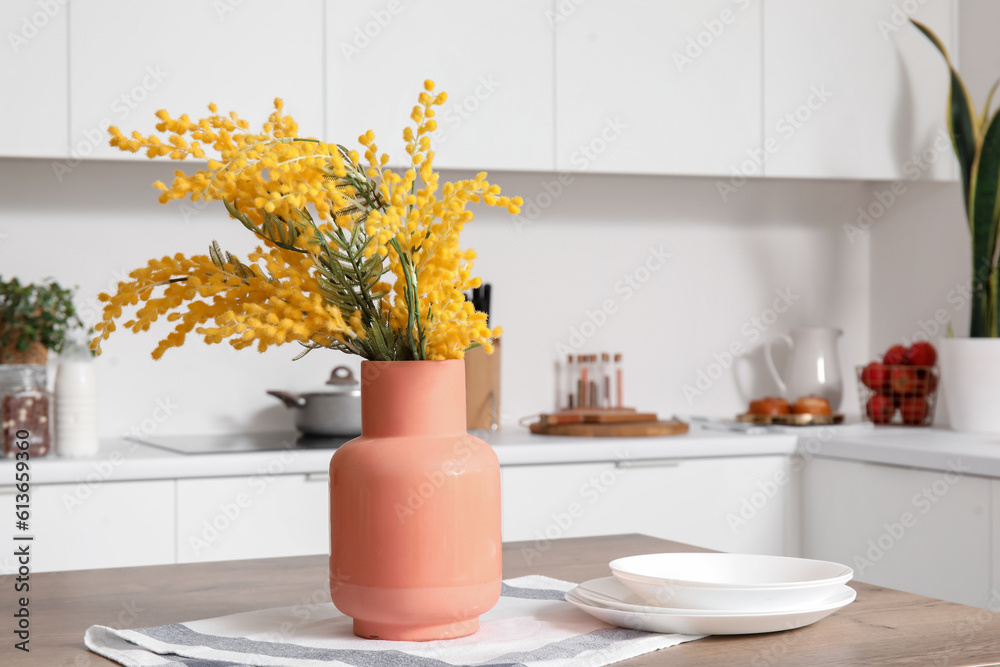 Vase with mimosa flowers on wooden table in modern kitchen