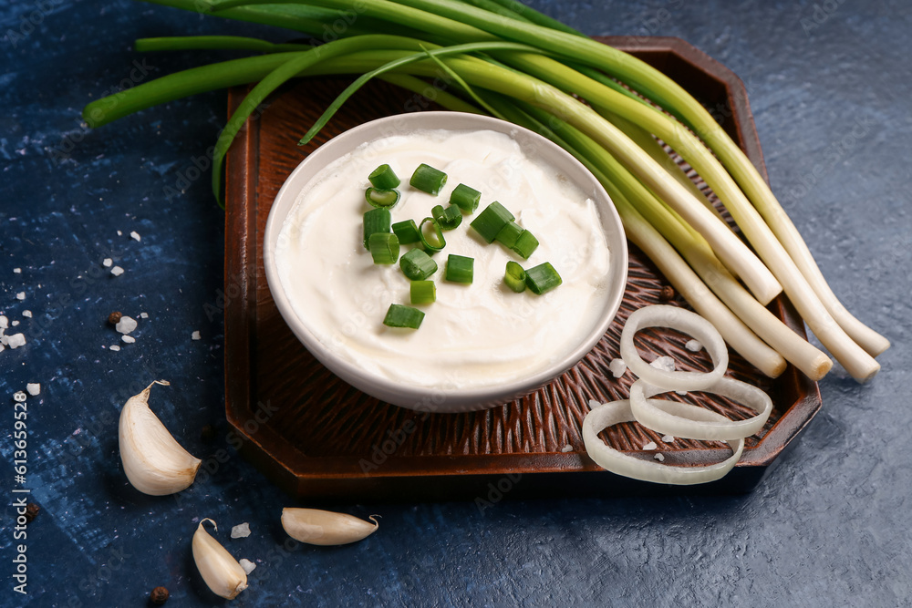 Bowl of tasty sour cream with scallion and onion on blue background