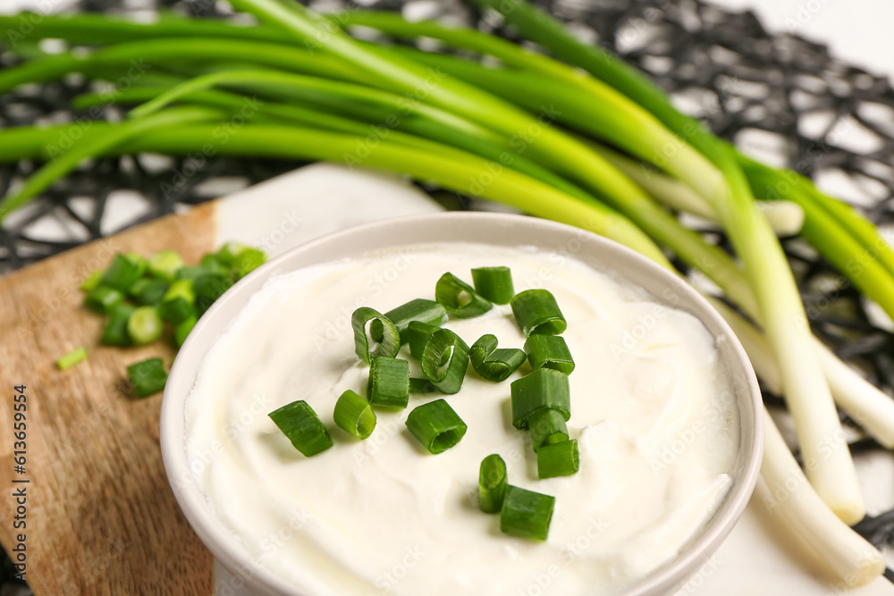 Board and bowl of tasty sour cream with sliced green onion, closeup