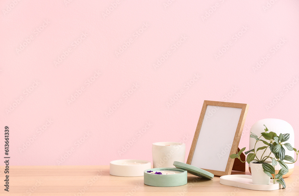 Holders with candles and blank frame on table near pink wall in room