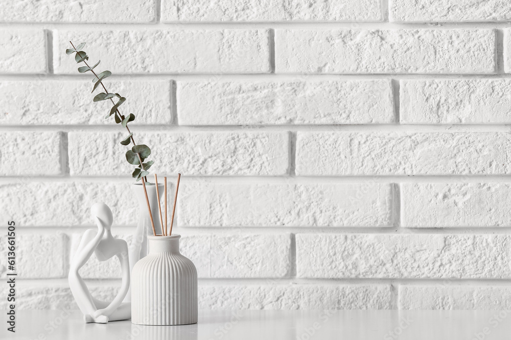 Bottle of reed diffuser and eucalyptus branch on table near light brick wall in room