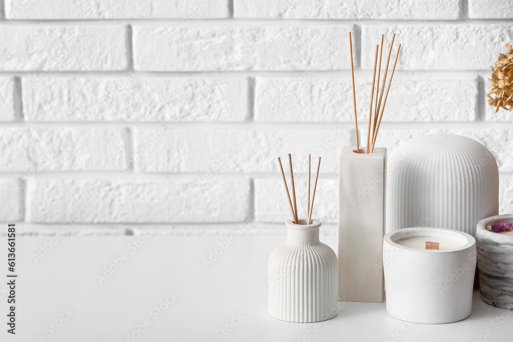 Bottles of reed diffuser and candles on table near light brick wall in room