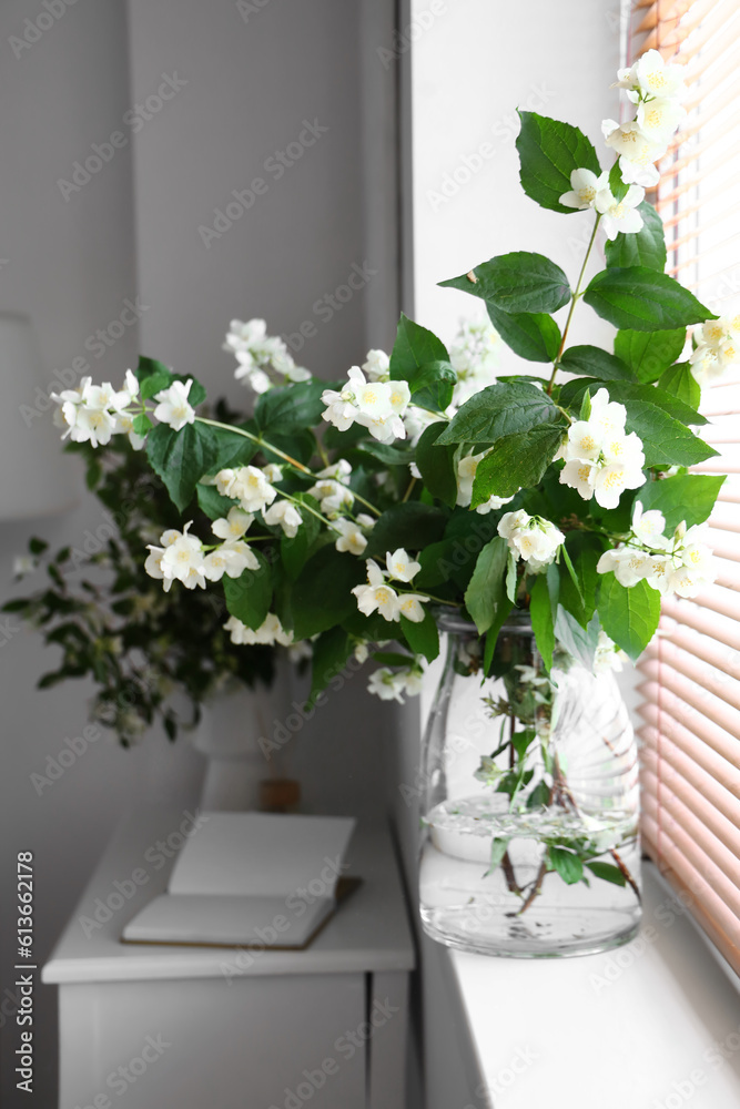 Vase with blooming jasmine flowers on windowsill, closeup