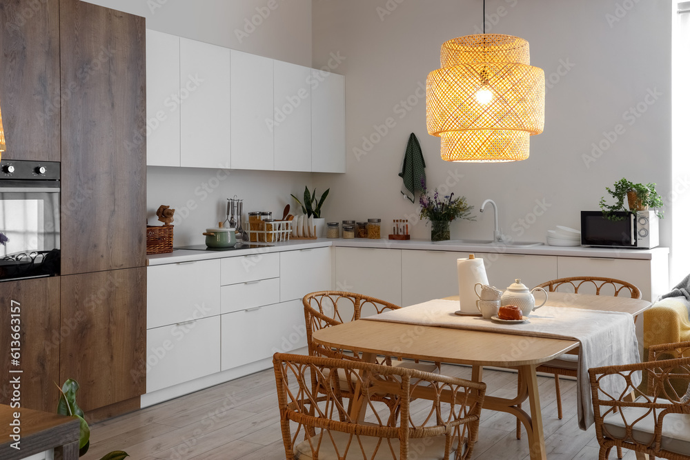 Interior of modern kitchen with glowing lamp and teapot on dining table