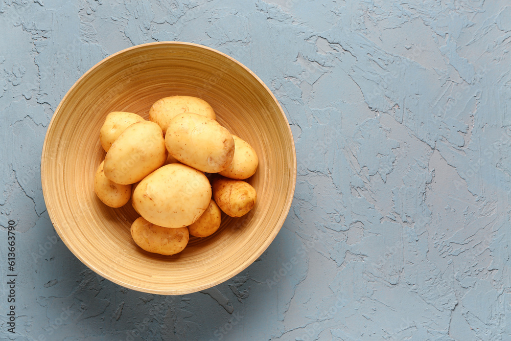 Bowl with raw baby potatoes on blue background