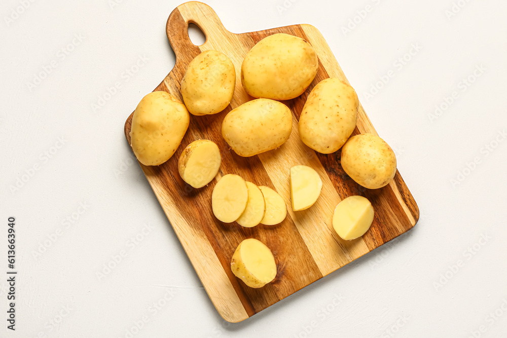 Wooden board with raw baby potatoes on white background