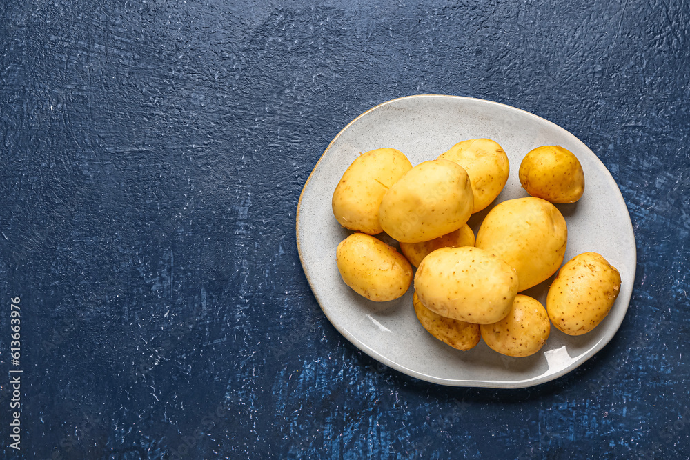 Plate with raw baby potatoes on blue background