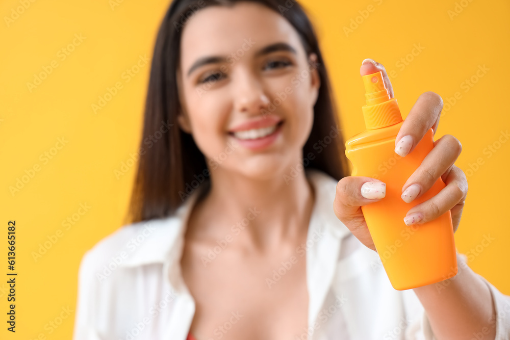 Young woman with sunscreen cream on yellow background, closeup