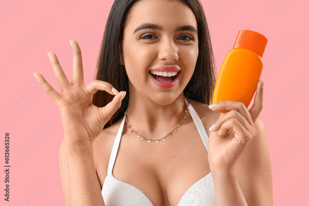 Young woman with sunscreen cream showing OK on pink background, closeup