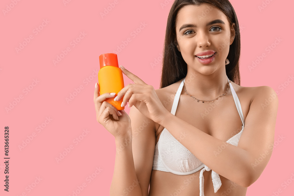 Young woman with sunscreen cream on pink background