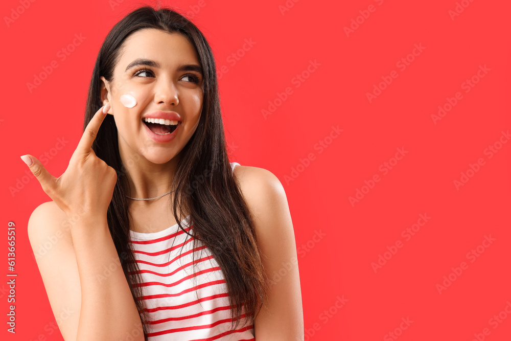 Young woman pointing at sunscreen cream on her face against red background