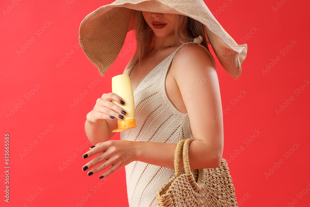 Young woman applying sunscreen cream on red background