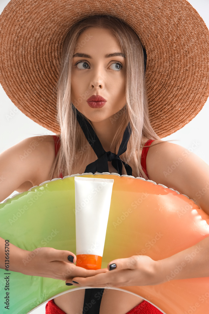 Thoughtful young woman with sunscreen cream and inflatable ring on light background, closeup