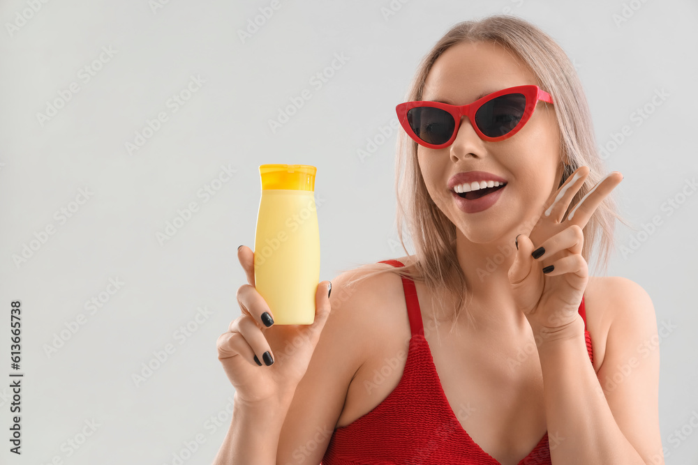 Young woman with sunscreen cream showing victory gesture on light background, closeup