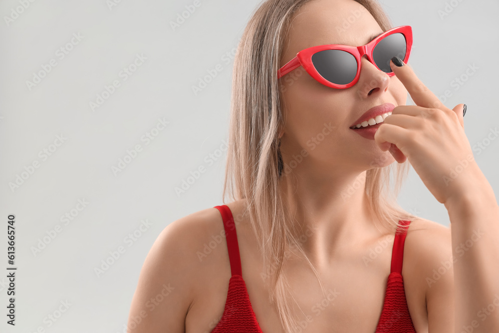 Young woman applying sunscreen cream on her nose against light background, closeup