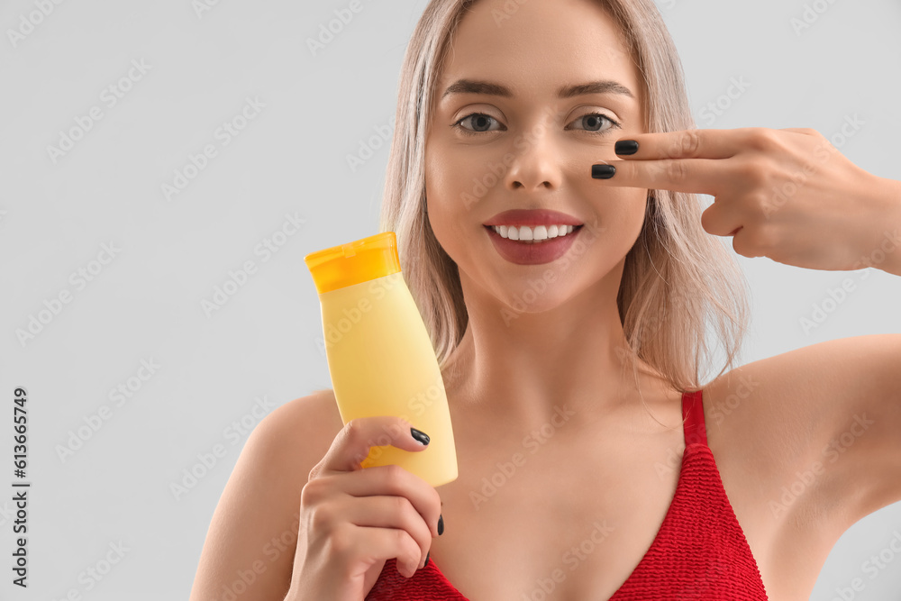 Young woman applying sunscreen cream on her face against light background, closeup