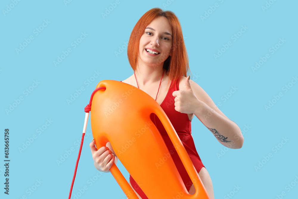 Female lifeguard with rescue buoy showing thumb-up on blue background