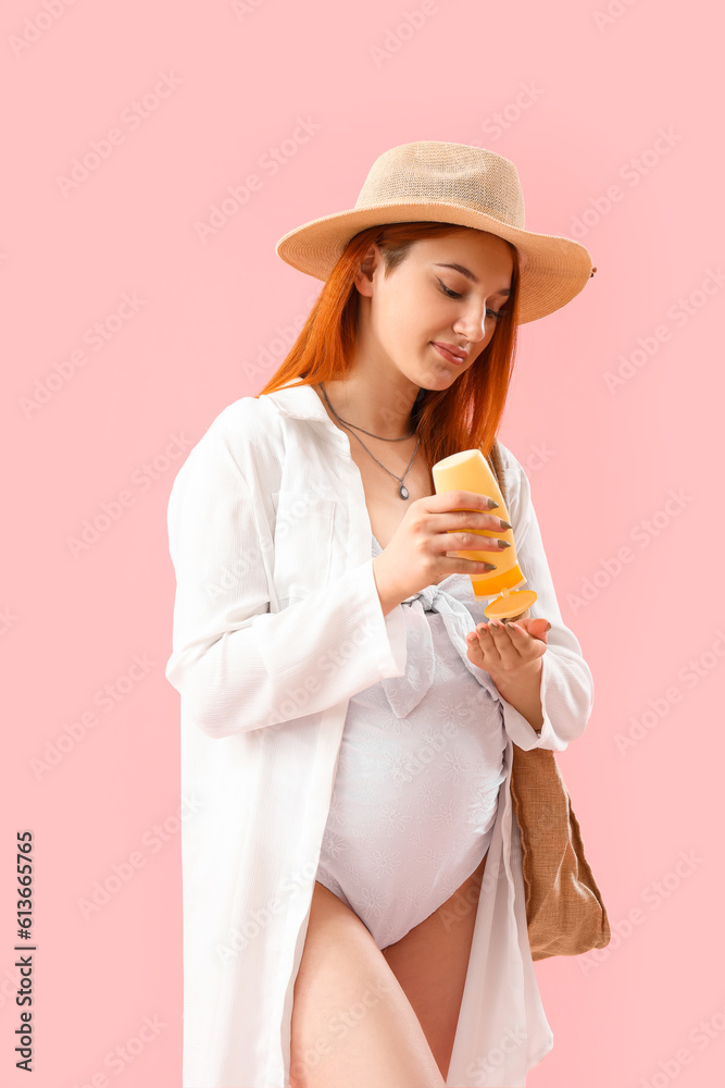 Young pregnant woman applying sunscreen cream on pink background