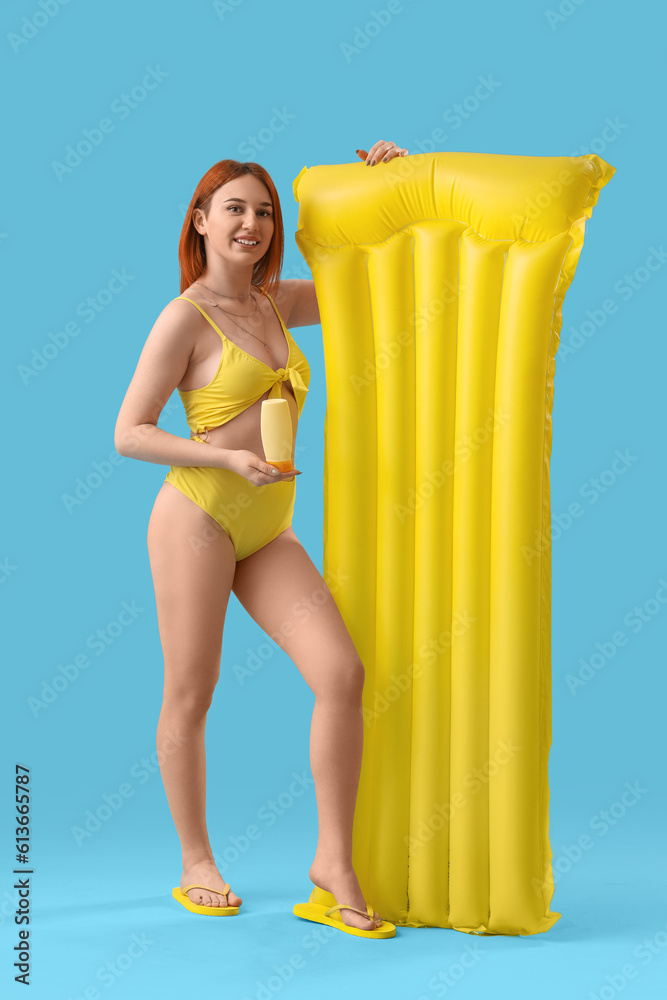 Young woman with sunscreen cream and inflatable mattress on blue background