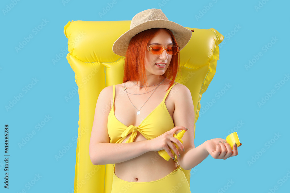 Young woman with sunscreen cream and inflatable mattress on blue background