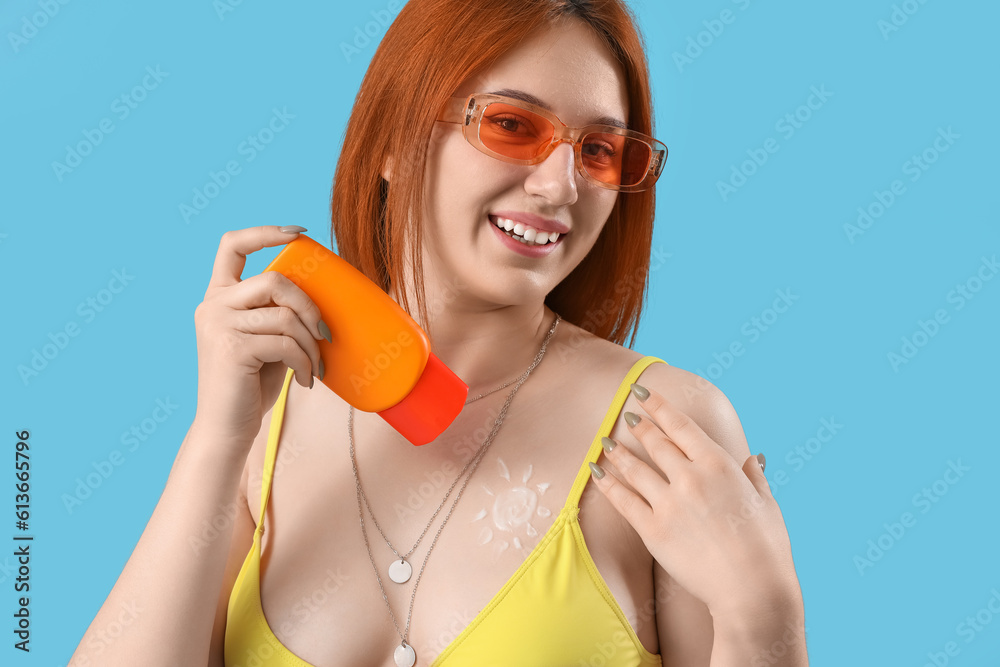 Young woman with sun made of sunscreen cream on blue background, closeup