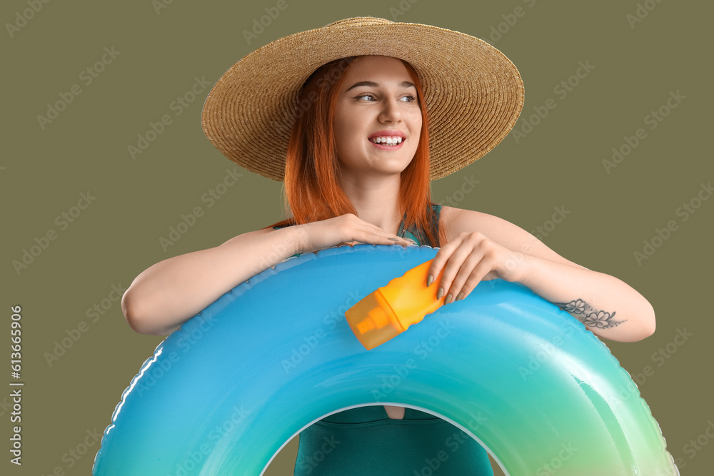 Young woman with sunscreen cream and inflatable ring on green background