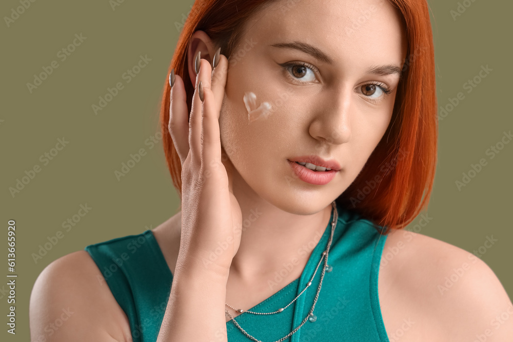 Young woman with heart made of sunscreen cream on green background, closeup