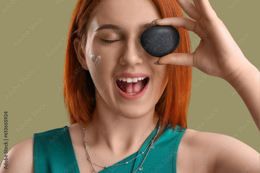 Young woman with heart made of sunscreen cream and pebble on green background, closeup