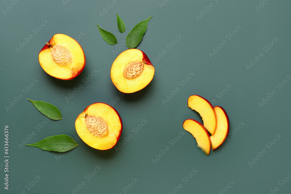 Halves of sweet peaches and leaves on green background