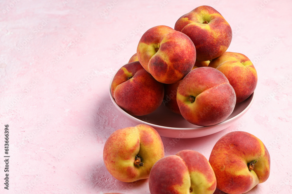 Bowl with sweet peaches on pink background