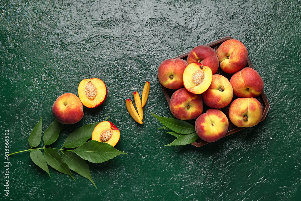 Tray with sweet peaches and leaves on green background