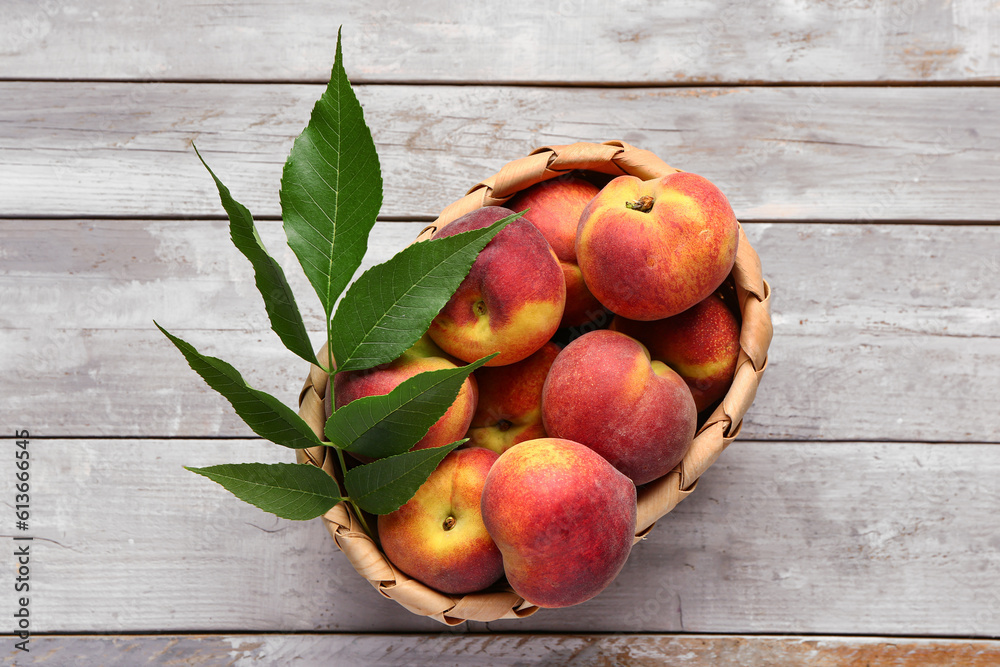 Wicker bowl with sweet peaches and leaves on grey wooden background