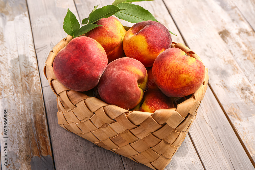 Wicker bowl with sweet peaches and leaves on grey wooden background