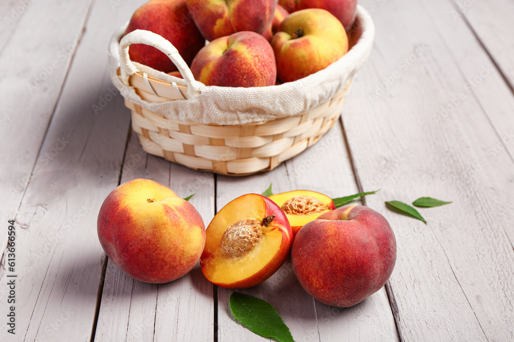 Wicker basket with sweet peaches and leaves on white wooden background