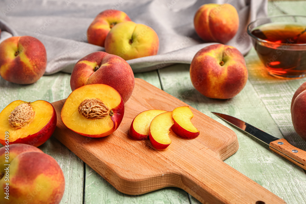 Board with cut sweet peaches on green wooden background