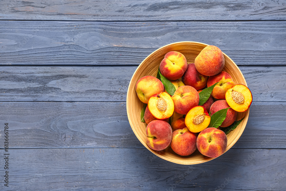 Bowl with sweet peaches and leaves on blue wooden background